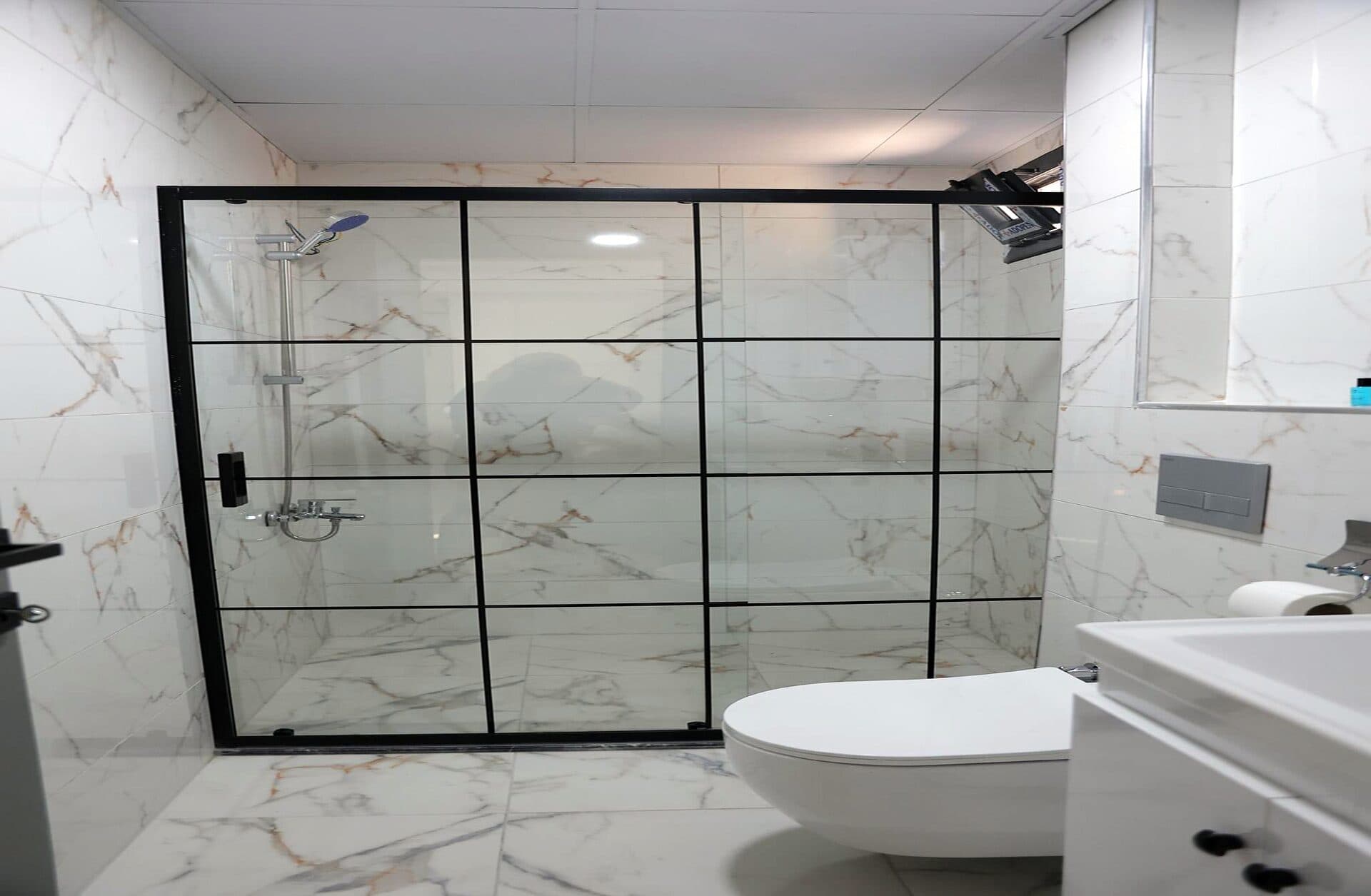 Siyah çerçeveli cam duş kabini olan mermer banyo